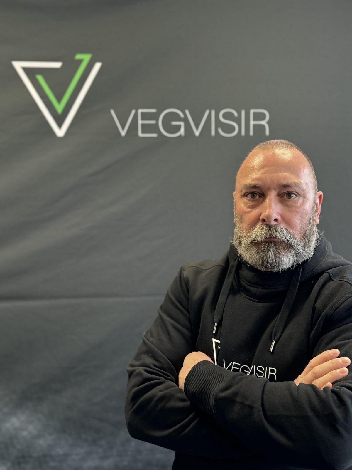 Portrait of Mark Boland in a Vegvisir hoodie, standing in front of the Vegvisir logo